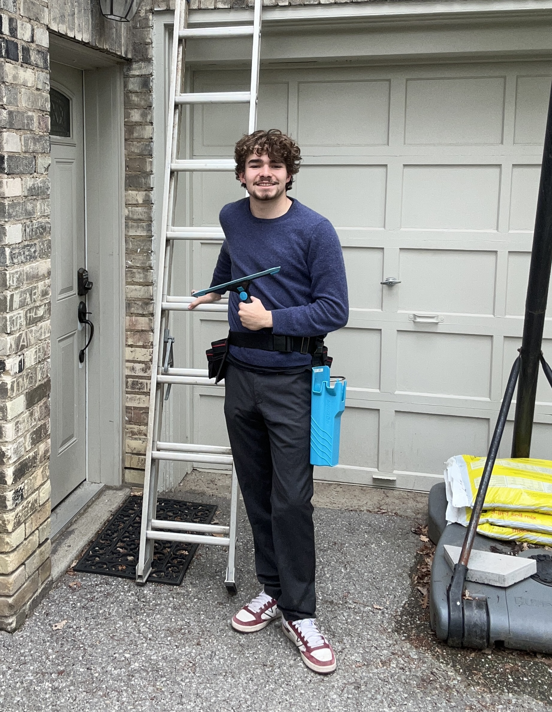 Iain Brady, owner of Brady's Window Washing Co., smiling with a squeegee in front of his ladder